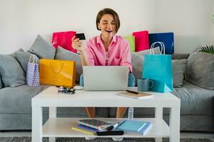 contento sorridente donna nel rosa camicia su divano a casa shopping in linea foto