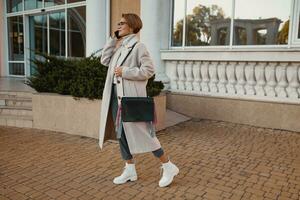 elegante alla moda donna a piedi nel strada nel elegante stile cappotto foto