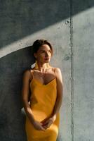 attraente donna nel giallo estate vestito nel interno camera calcestruzzo parete sfondo foto