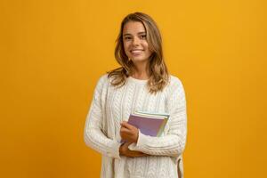 giovane sorridente bella biondo donna in posa con libri su giallo studio sfondo isolato, contento formazione scolastica, indossare bianca maglione foto