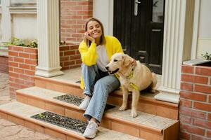 contento sorridente donna nel giallo maglione a piedi a sua Casa con un' cane d'oro cane da riporto foto