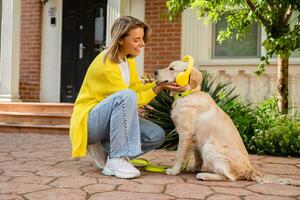 donna nel giallo maglione a piedi a sua Casa con un' cane ascoltando per musica nel cuffie foto