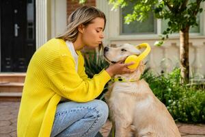 donna nel giallo maglione a piedi a sua Casa con un' cane ascoltando per musica nel cuffie foto