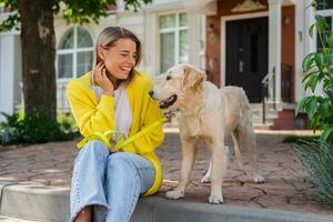 contento sorridente donna nel giallo maglione a piedi a sua Casa con un' cane d'oro cane da riporto foto
