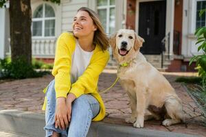 contento sorridente donna nel giallo maglione a piedi a sua Casa con un' cane d'oro cane da riporto foto