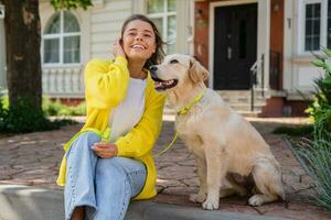 contento sorridente donna nel giallo maglione a piedi a sua Casa con un' cane d'oro cane da riporto foto