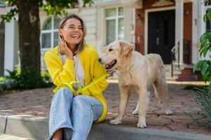 contento sorridente donna nel giallo maglione a piedi a sua Casa con un' cane d'oro cane da riporto foto
