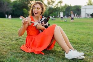 giovane contento sorridente donna nel arancia vestito avendo divertimento giocando con cane nel parco foto