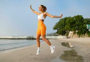 bella giovane sorridente donna fare gli sport nel il mattina nel elegante sport attrezzatura abbigliamento sportivo, magro forte corpo, salutare in forma stile di vita foto