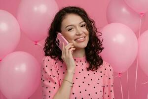 bella giovane donna in posa isolato su rosa studio sfondo con rosa aria baloons e smartphone foto