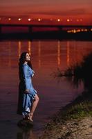bella ragazza con lunghi capelli ondulati scuri in piedi sulla riva del fiume foto