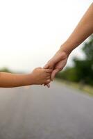 mani di un' madre e bambino camminare mano nel mano su il strada. sotto il sera sole foto