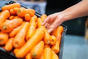 mano della donna che prende la carota in supermercato. donna shopping in un supermercato e l'acquisto di verdure fresche biologiche. concetto di alimentazione sana.
