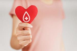 le mani della donna che tengono il cuore rosso con il segno del donatore di sangue. concetto di assistenza sanitaria, medicina e donazione di sangue foto