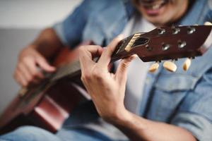 goditi un bell'uomo asiatico che si esercita o suona la chitarra sul divano del soggiorno foto