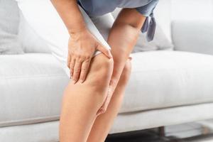 primo piano di una donna paffuta seduta sul divano e che sente dolore al ginocchio e si massaggia il ginocchio. concetto di assistenza sanitaria e medica. foto