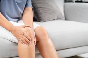 primo piano di una donna paffuta seduta sul divano e che sente dolore al ginocchio e si massaggia il ginocchio. concetto di assistenza sanitaria e medica. foto