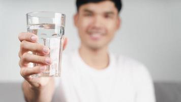 bell'uomo asiatico che beve un bicchiere d'acqua sul divano del soggiorno foto