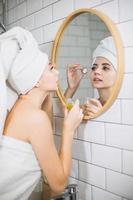 giovane donna in un asciugamano bianco applica olio idratante sulla pelle del viso. foto