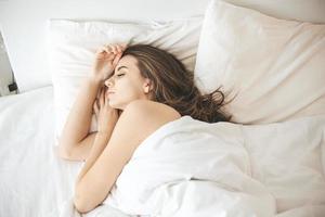 giovane donna che dorme pacificamente in camera da letto con lenzuola bianche fresche foto