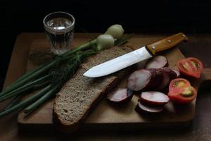 cibo semplice rustico. salsiccia, pomodoro, coltello e pane. foto