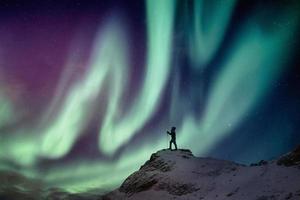 scalatore uomo in piedi sulla vetta innevata con aurora boreale e stellato foto