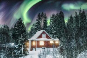 aurora boreale sopra la casa nordica rossa con la neve in inverno di notte foto