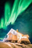 aurora boreale aurora boreale su casa bianca illuminata su neve in inverno foto