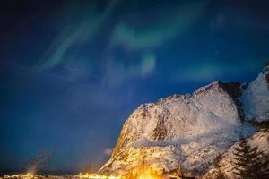 aurora boreale sopra la montagna di neve nella città di reine alle isole lofoten foto
