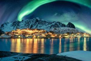 aurora boreale oltre l'illuminazione del villaggio di pescatori sulla costa in inverno alle isole lofoten foto