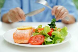 asiatico anziano donna paziente mangiare salmone palo e verdura insalata per salutare cibo nel Ospedale. foto