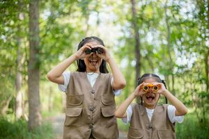 contento poco asiatico ragazze guardare avanti e sorridente bambino con il binocolo nel il parco. viaggio e avventura concetto. libertà, vacanza foto