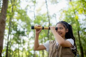 contento poco asiatico ragazze guardare avanti e sorridente bambino con il binocolo nel il parco. viaggio e avventura concetto. libertà, vacanza foto