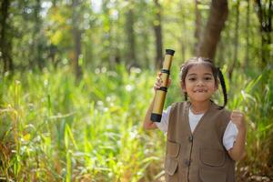 asiatico poco ragazze Esplorare natura attraverso ingrandimento bicchieri e binocolo nel il parco. formazione scolastica, campo viaggi, ricerca, e scoperta concetti. foto