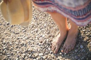 avvicinamento foto di un' ragazze gambe nel un' gonna nel ciottoli e sabbia su il spiaggia