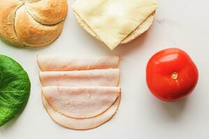 cibo prodotti e ingredienti per fabbricazione Sandwich. prosciutto, formaggio, hamburger panino, lattuga, cetriolo e pomodoro come ricetta flatlay su marmo cucina tavolo foto