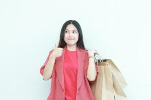 ritratto di bellissimo asiatico donna indossare rosso attrezzatura Esprimere a gesti trasporto molte di shopping borse con contento espressione foto