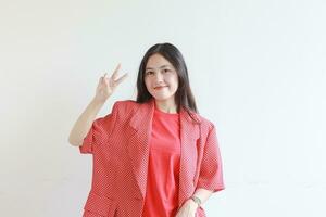ritratto di bellissimo asiatico donna indossare rosso attrezzatura con mano gesto senso pace foto