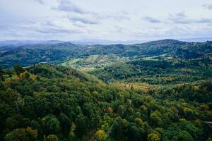 frone volo al di sopra di montagna paesaggio con autunno foresta. montagna villaggio foto