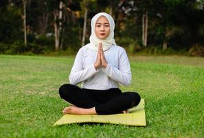 giovane donna musulmana asiatica seduta sull'erba, godendosi la meditazione foto