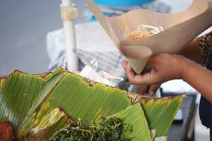 un' donna è preparazione kluban riso per acquirenti.kluban è un' varietà di verdure bollito e condito con grattugiato Noce di cocco. foto