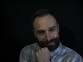 un uomo con barba e baffi con una faccia premurosa e sorniona su uno sfondo nero foto