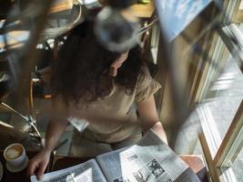una ragazza con i capelli ricci siede al tavolo di un bar e legge un giornale foto