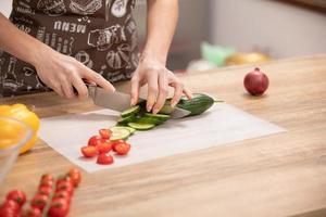 le mani della donna che tagliano il cetriolo, dietro le verdure fresche. foto