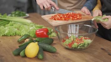 Immagine ravvicinata delle mani dell'uomo che affettano le verdure sul tagliere di legno per insalata sul tavolo con cibo sano in cucina.
