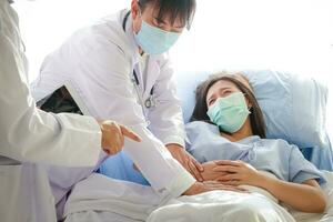 Due asiatico medici esaminato il addominale dolore di un' donna dire bugie nel un' ospedale letto. trattamento di pazienti durante il coronavirus epidemico. concetto di medico servizio foto