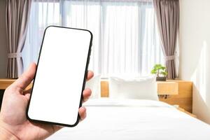 avvicinamento di femmina uso mano Tenere smartphone sfocato immagini di sfocato bianca cuscino su letto decorazione con leggero lampada nel Hotel Camera da letto interno sfondo, tempo libero e viaggio nel il vacanza concetto foto