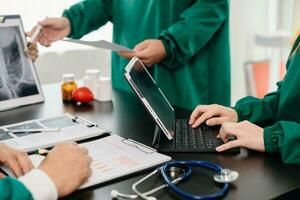 medico squadra avendo un' incontro con medici nel bianca laboratorio cappotti e chirurgico scrub seduto a un' tavolo discutere un' pazienti Lavorando in linea utilizzando computer nel il medico foto