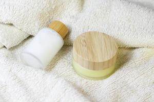 spazzola naturale in legno per il massaggio della pelle secca su asciugamano bianco con flaconi cosmetici in cristallo con piano in legno di bambù