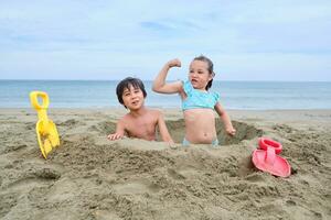 bambini scavare un' buco nel il sabbia su il spiaggia. foto